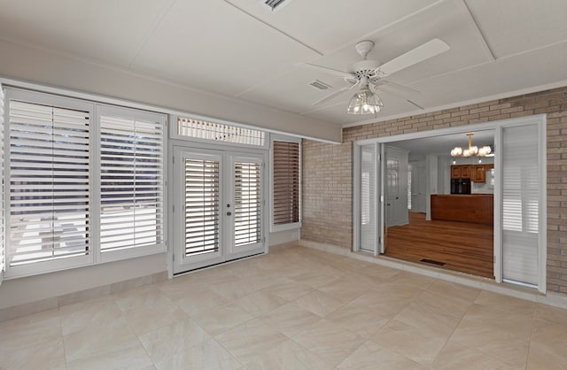 empty room with french doors, ceiling fan with notable chandelier, and brick wall