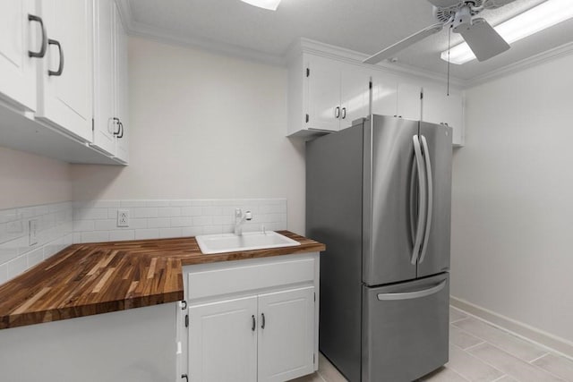 kitchen featuring stainless steel refrigerator, white cabinetry, sink, ceiling fan, and butcher block countertops