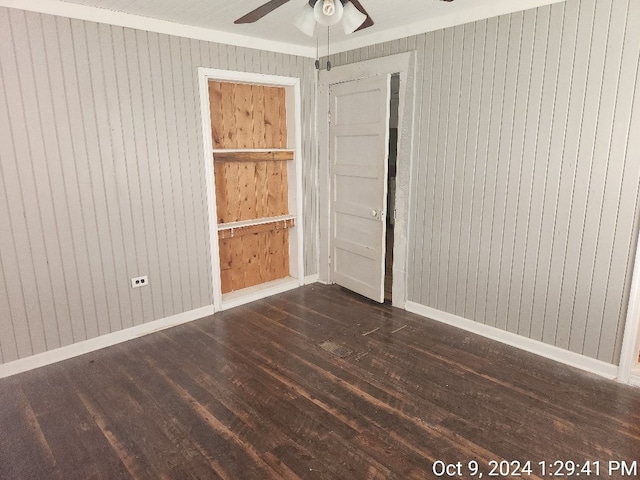 empty room with ceiling fan, wood walls, dark hardwood / wood-style flooring, and crown molding