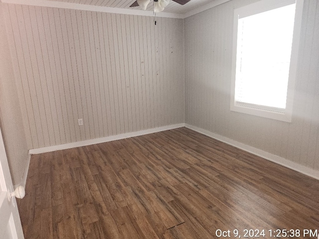 empty room featuring dark hardwood / wood-style flooring, wooden walls, ceiling fan, and ornamental molding