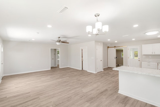 unfurnished living room with ceiling fan with notable chandelier, a barn door, and light hardwood / wood-style flooring