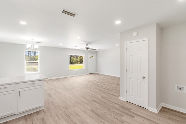 unfurnished living room with ceiling fan with notable chandelier, a healthy amount of sunlight, and light hardwood / wood-style floors