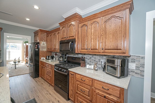 kitchen featuring light stone countertops, light wood-type flooring, backsplash, crown molding, and black appliances