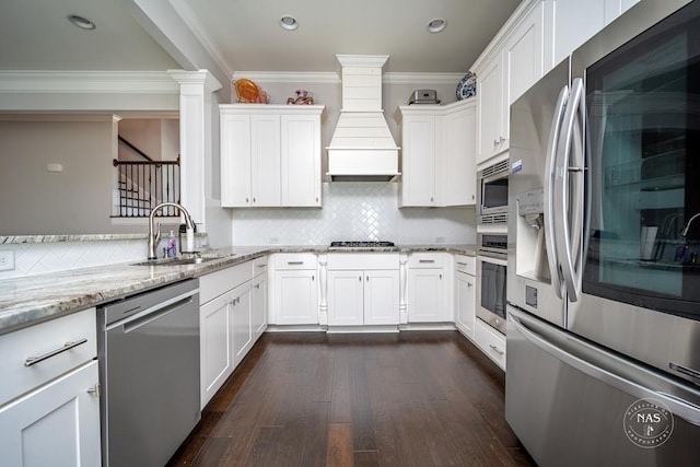 kitchen with appliances with stainless steel finishes, light stone counters, custom range hood, dark wood-type flooring, and white cabinets