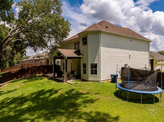 rear view of property with a yard, a trampoline, and a patio