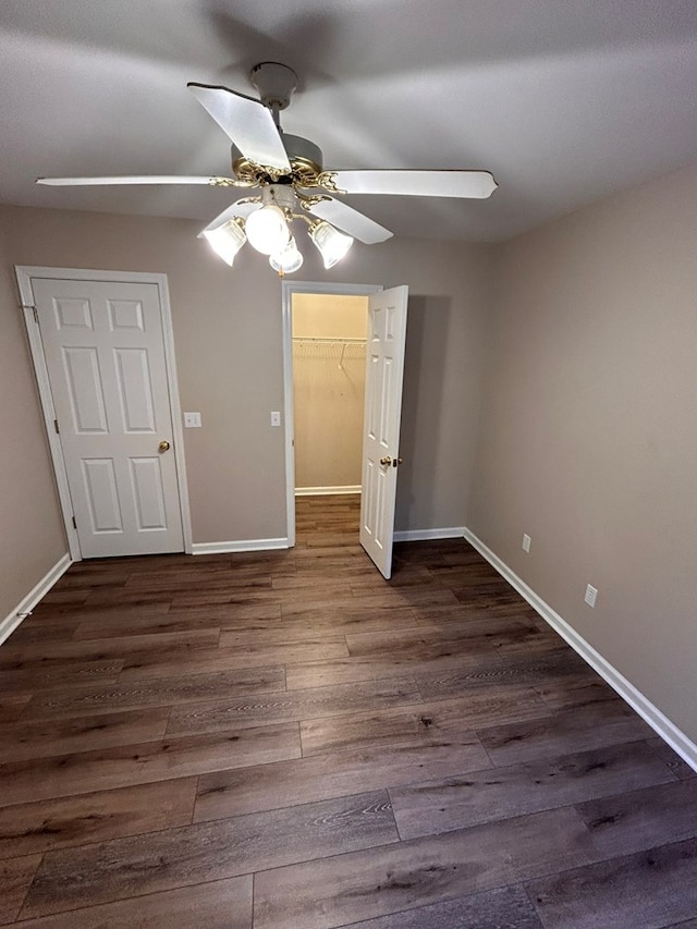 unfurnished bedroom featuring ceiling fan, a walk in closet, dark wood-type flooring, and a closet