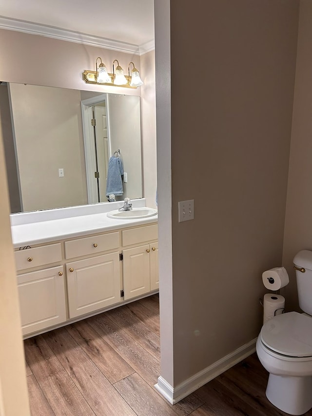 bathroom featuring vanity, toilet, wood-type flooring, and ornamental molding