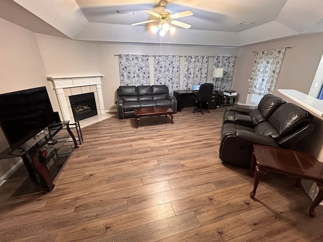 living room with a fireplace, wood-type flooring, a raised ceiling, and ceiling fan