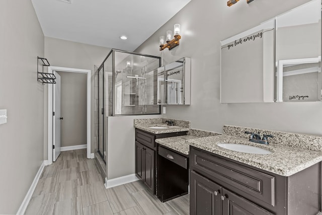 full bath featuring two vanities, a shower stall, baseboards, and a sink