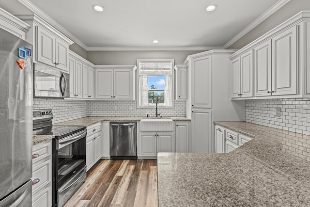 kitchen with backsplash, appliances with stainless steel finishes, wood finished floors, and a sink