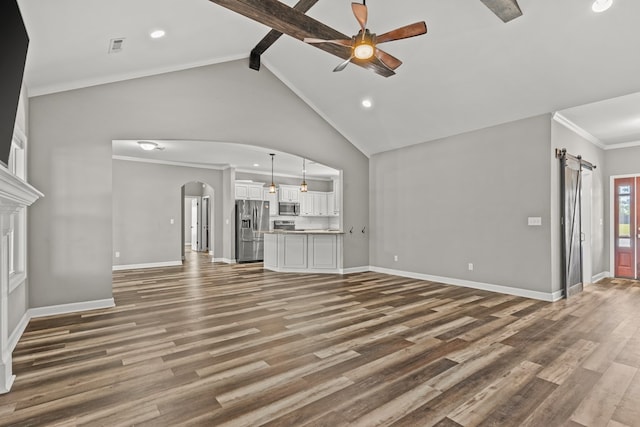 unfurnished living room with arched walkways, a barn door, beamed ceiling, a ceiling fan, and wood finished floors