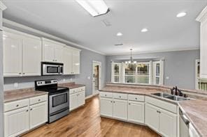 kitchen with white cabinets, appliances with stainless steel finishes, ornamental molding, light wood-style floors, and a sink