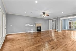 unfurnished living room with ceiling fan with notable chandelier, a fireplace, wood finished floors, and baseboards