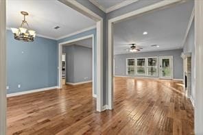 unfurnished living room with ceiling fan with notable chandelier, a fireplace, wood finished floors, baseboards, and ornamental molding