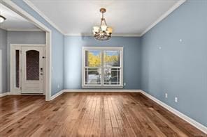 unfurnished dining area with crown molding, a notable chandelier, baseboards, and wood finished floors