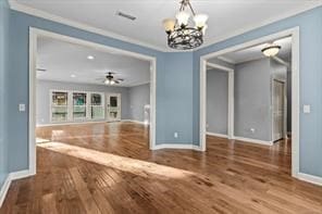 unfurnished living room featuring baseboards, visible vents, crown molding, and wood finished floors