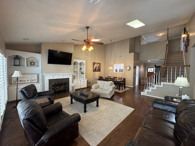 living area with a fireplace with flush hearth, wood finished floors, baseboards, stairs, and ceiling fan