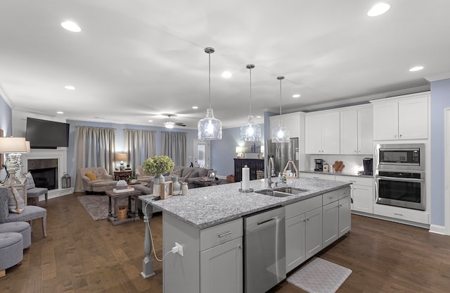 kitchen with light stone counters, a kitchen island with sink, white cabinetry, a fireplace, and appliances with stainless steel finishes