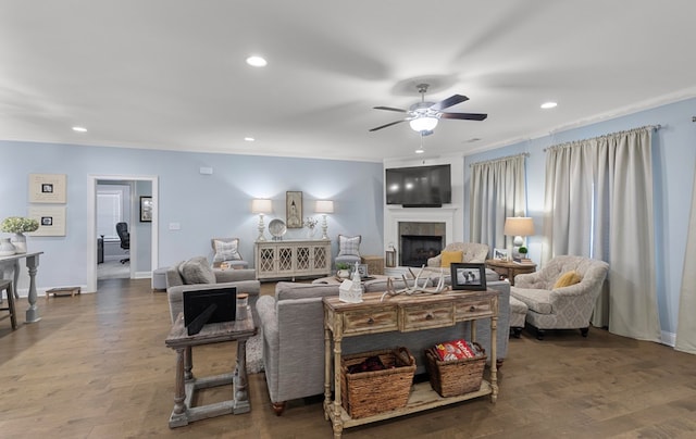 living room with a tiled fireplace, ceiling fan, crown molding, and dark hardwood / wood-style flooring