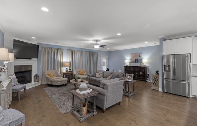 living room featuring a tiled fireplace, dark hardwood / wood-style flooring, ornamental molding, and ceiling fan