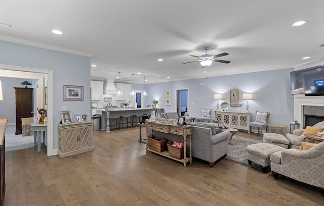 living room with a tiled fireplace, ceiling fan, crown molding, and dark hardwood / wood-style floors