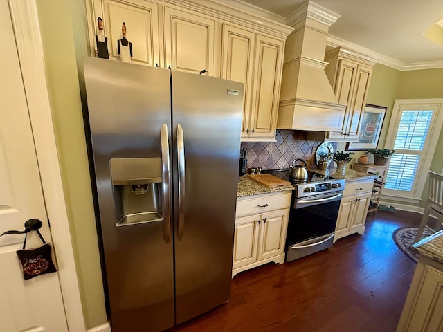 kitchen with light stone counters, ornamental molding, stainless steel appliances, dark wood-type flooring, and cream cabinetry