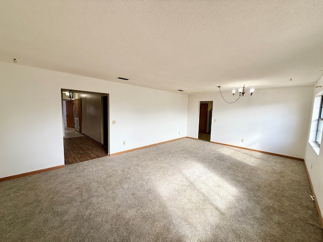 empty room featuring a textured ceiling, a chandelier, and dark colored carpet