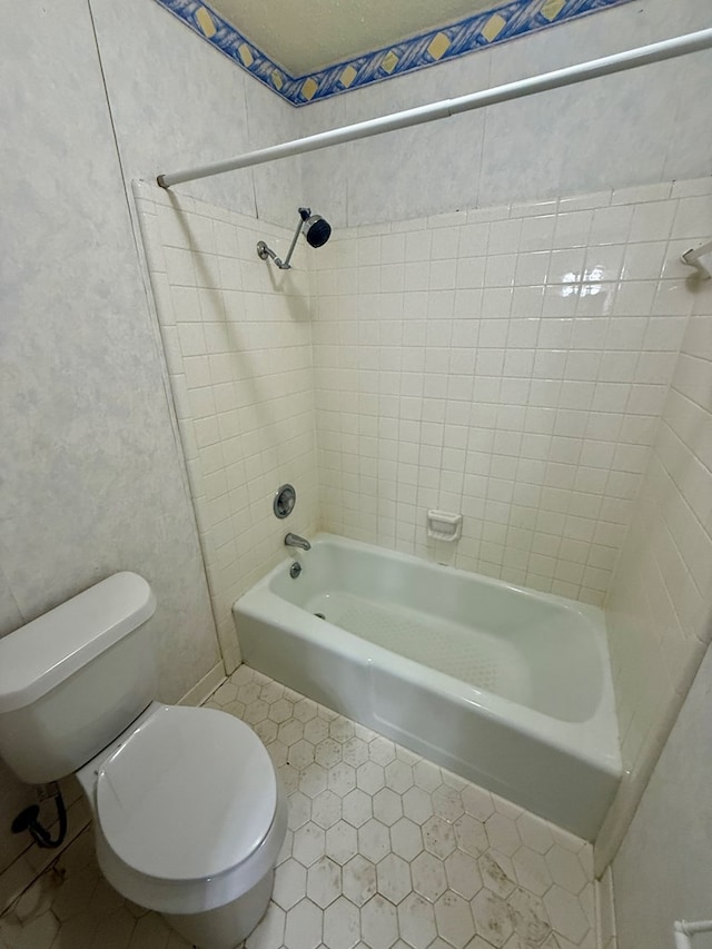 bathroom with toilet, tiled shower / bath, and tile patterned flooring