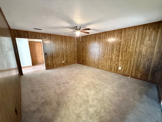 spare room with ceiling fan, light colored carpet, wood walls, and a textured ceiling