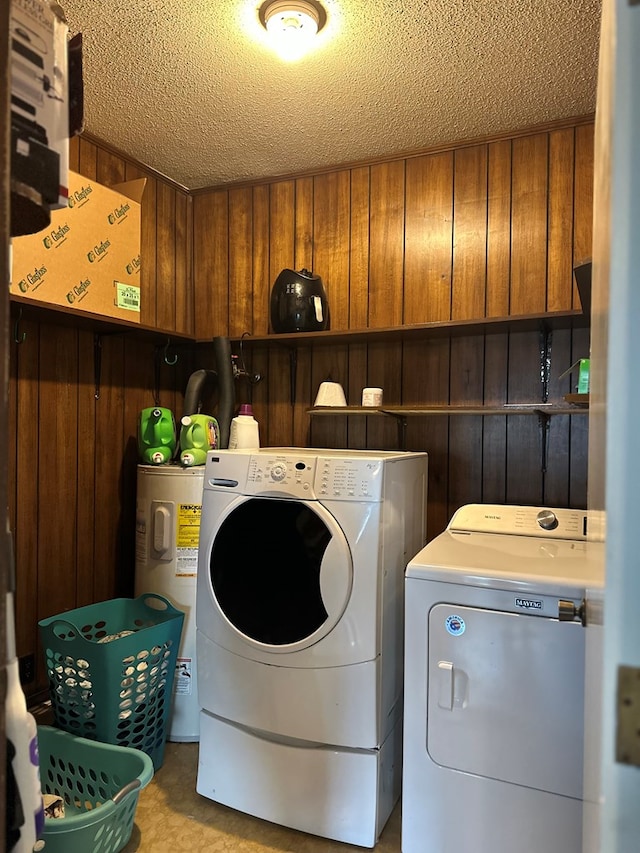 laundry area with wooden walls, water heater, laundry area, a textured ceiling, and separate washer and dryer