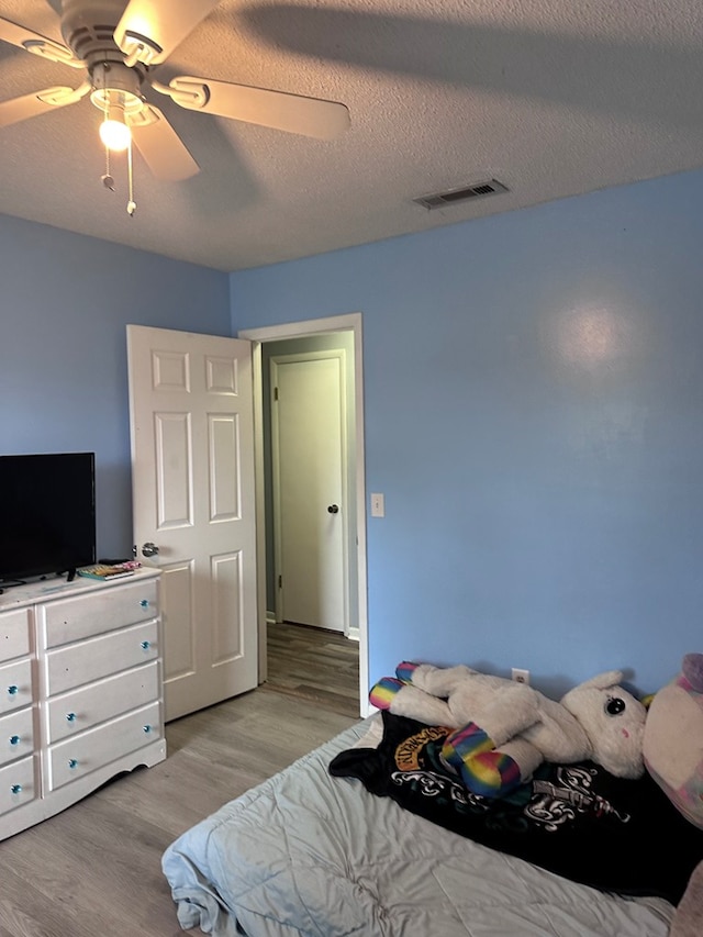 bedroom featuring ceiling fan, wood finished floors, visible vents, and a textured ceiling