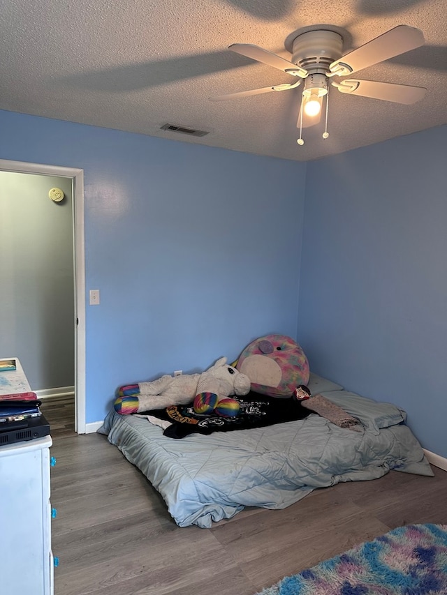 bedroom featuring visible vents, a textured ceiling, a ceiling fan, and wood finished floors