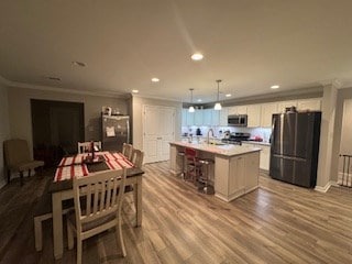 kitchen featuring a kitchen island with sink, stainless steel appliances, light wood-type flooring, hanging light fixtures, and white cabinets