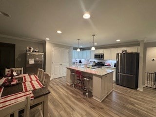 kitchen with decorative light fixtures, white cabinetry, wood-type flooring, a kitchen island, and appliances with stainless steel finishes