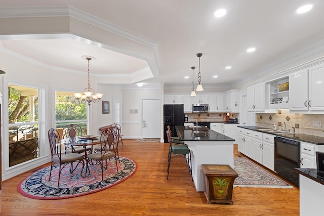 kitchen with light hardwood / wood-style floors, decorative light fixtures, a center island with sink, white cabinets, and black appliances