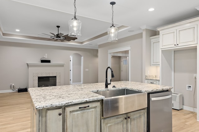 kitchen featuring a center island with sink, light hardwood / wood-style floors, a raised ceiling, and stainless steel dishwasher