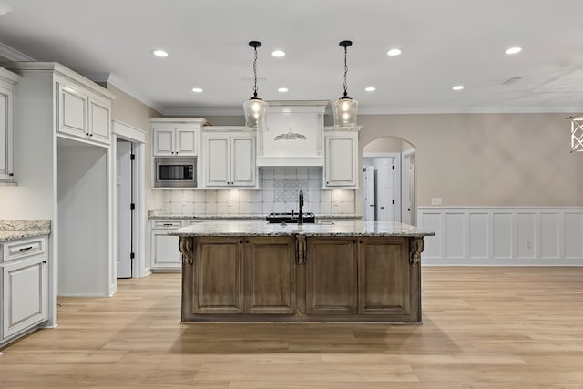 kitchen featuring a center island with sink, decorative light fixtures, stainless steel microwave, and light stone counters