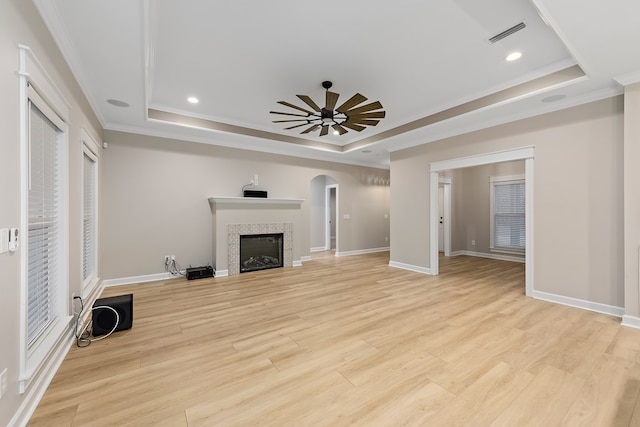 unfurnished living room featuring light wood-type flooring, a raised ceiling, ceiling fan, and crown molding