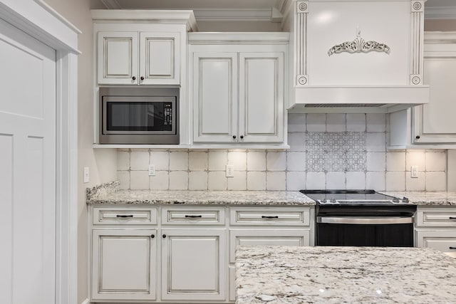 kitchen with appliances with stainless steel finishes, backsplash, ornamental molding, custom range hood, and white cabinetry