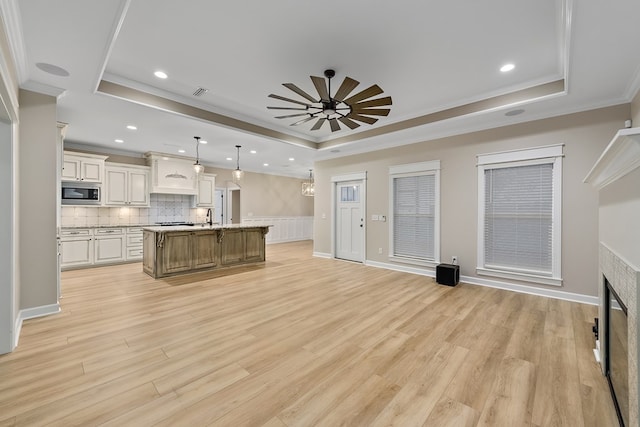 kitchen with a center island with sink, decorative light fixtures, stainless steel microwave, and a tray ceiling