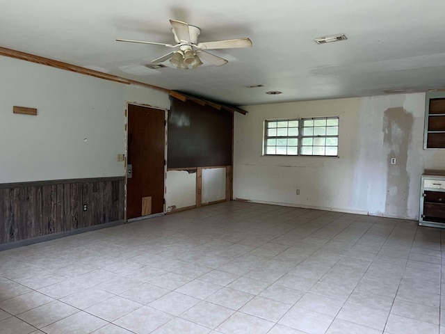 empty room featuring wooden walls, visible vents, a ceiling fan, and a wainscoted wall