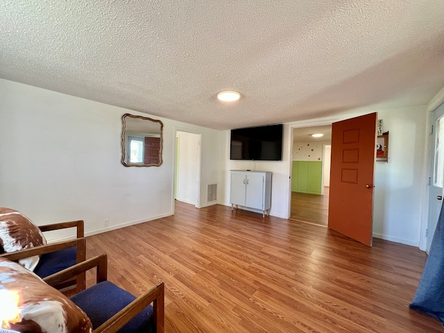 living room featuring visible vents, a textured ceiling, light wood-type flooring, and baseboards