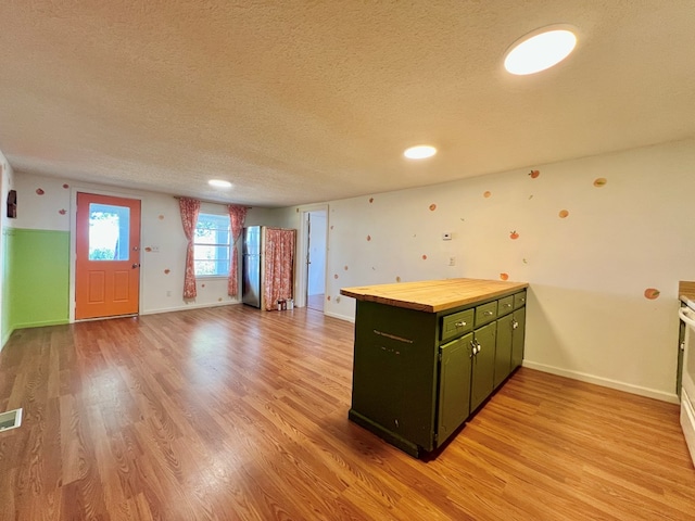 kitchen featuring light wood-style flooring, a textured ceiling, a peninsula, green cabinets, and wooden counters