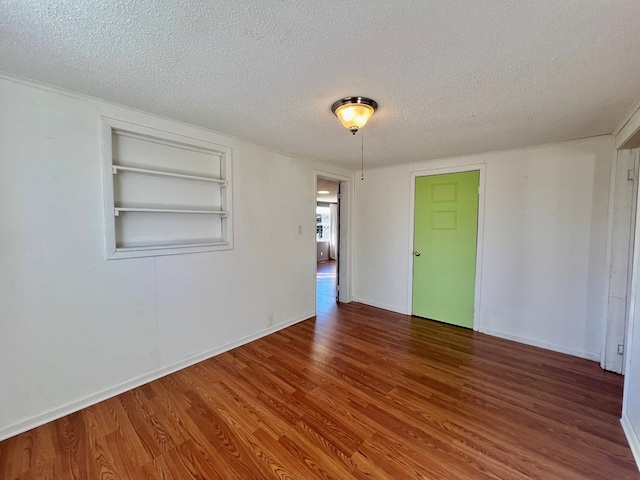 unfurnished room with built in features, baseboards, a textured ceiling, and wood finished floors