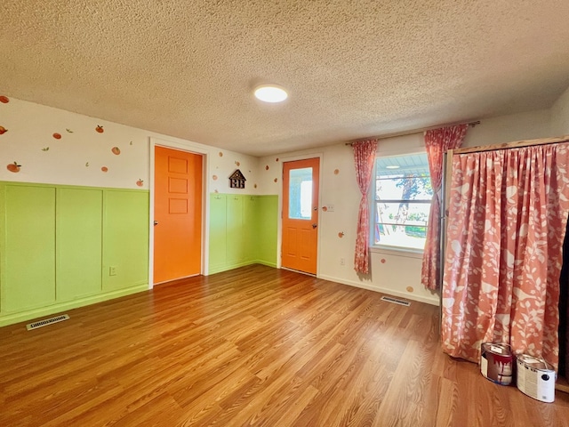 empty room featuring visible vents, baseboards, a textured ceiling, and light wood finished floors