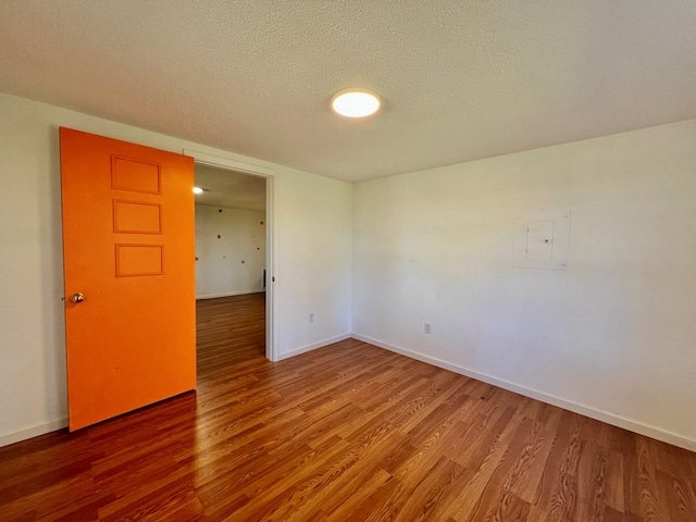 empty room with a textured ceiling, baseboards, and wood finished floors