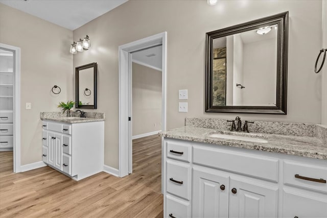 bathroom with baseboards, a sink, wood finished floors, and two vanities