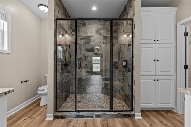 full bath featuring baseboards, a stall shower, toilet, and wood finished floors