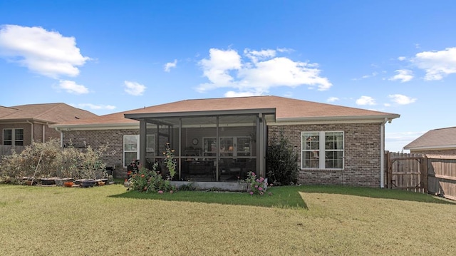 back of house featuring brick siding, a lawn, fence, and a sunroom