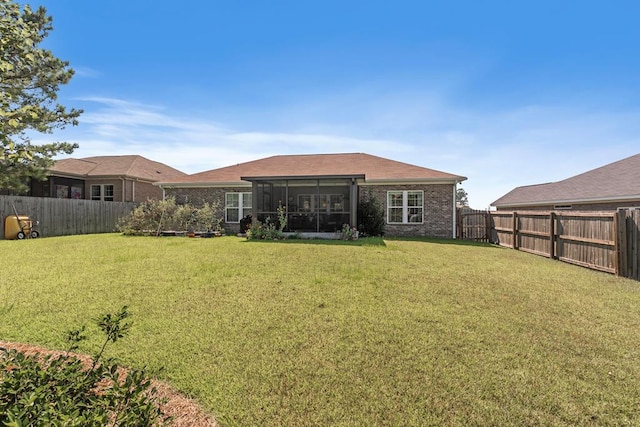 rear view of house featuring a sunroom, a fenced backyard, a lawn, and brick siding